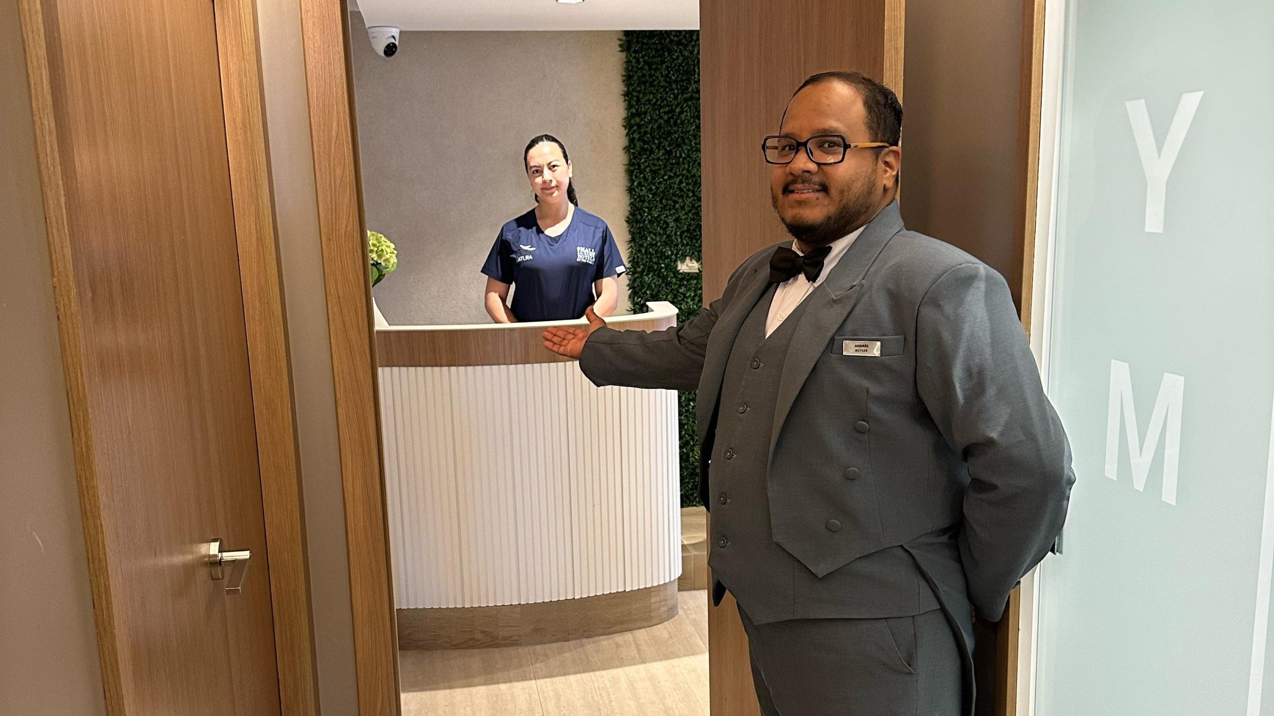 A butler aboard the luxury mega catamaran Hermes escorts a guest to the spa for a personalized massage appointment, where a therapist awaits at the reception.