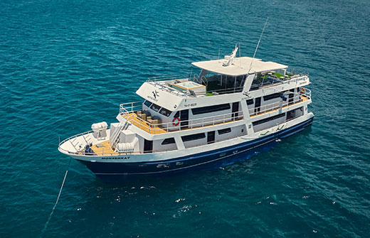 Aerial view of the Monserrat yacht cruising the turquoise waters of a Galapagos charter route.