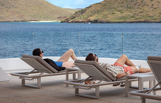 Guests relaxing on sun loungers aboard the Hermes Mega-catamaran during a Galapagos charter vacation.
