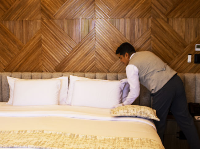A professional butler meticulously preparing a premium bed in a wood-paneled suite on an ultra-luxury cruise in the Galapagos.