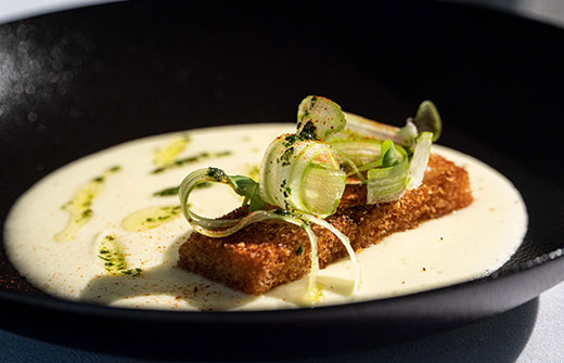 Close-up of a gourmet 5-course dish with delicate garnishes, showcasing the fine dining experience on an ultra-luxury cruise.