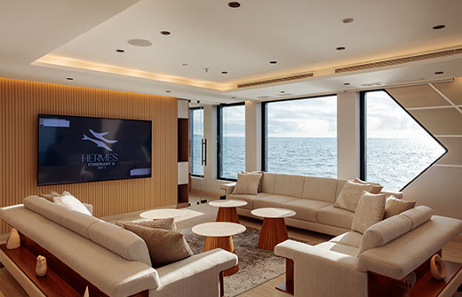 The spacious main lounge of the Hermes Mega Catamaran featuring panoramic windows and plush seating on an ultra-luxury cruise.