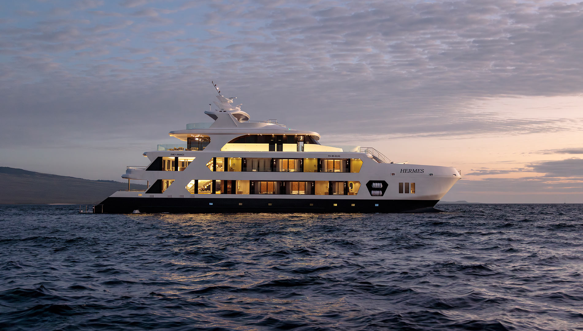 Side view of the ultra-luxury Hermes Mega Catamaran sailing at sunset in the Galapagos, with the sky full of vibrant colors.